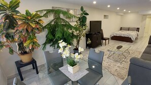 Ein modernes Wohnzimmer mit Glastisch, einer Couch, einem Bett und mehreren Blumentöpfen.