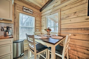 A wooden cabin interior with a dining table set for four, a coffee maker, and a trash can.