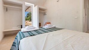 A bedroom with a bed, a bench, a towel rack, and a view of the outdoors. - 2499 Trulli La Meringa by Perle di Puglia (Ostuni)