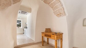 A narrow hallway with a wooden table and a lamp, leading to a kitchen area. - 2499 Trulli La Meringa by Perle di Puglia (Ostuni)