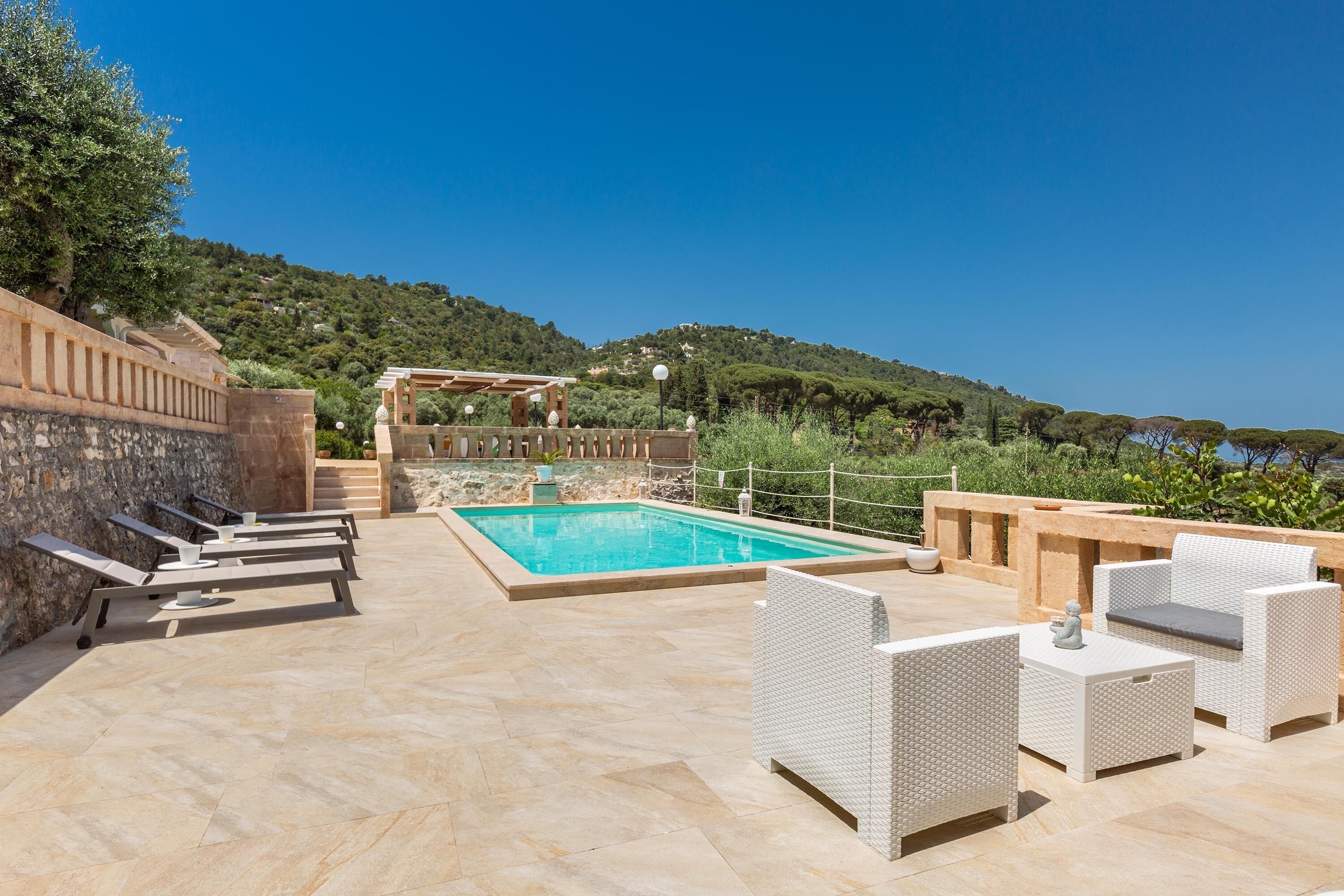 Un espace piscine doté de chaises longues et d’une pergola offrant une vue sur une colline.