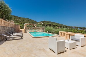 Zona de piscina amb gandules i una pèrgola amb vista a una collada.