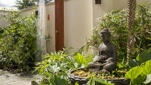 A statue of Buddha in a garden with a water feature and lush greenery. - Anoa Maresias Studios (São Sebastião)