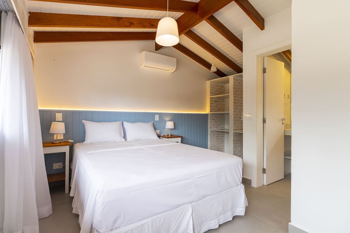 A bedroom with a large bed, a nightstand, a lamp, a wardrobe, and an open door leading to another room.