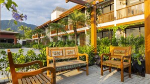 A courtyard with wooden benches, a covered walkway, and lush greenery. - Anoa Maresias Studios (São Sebastião)