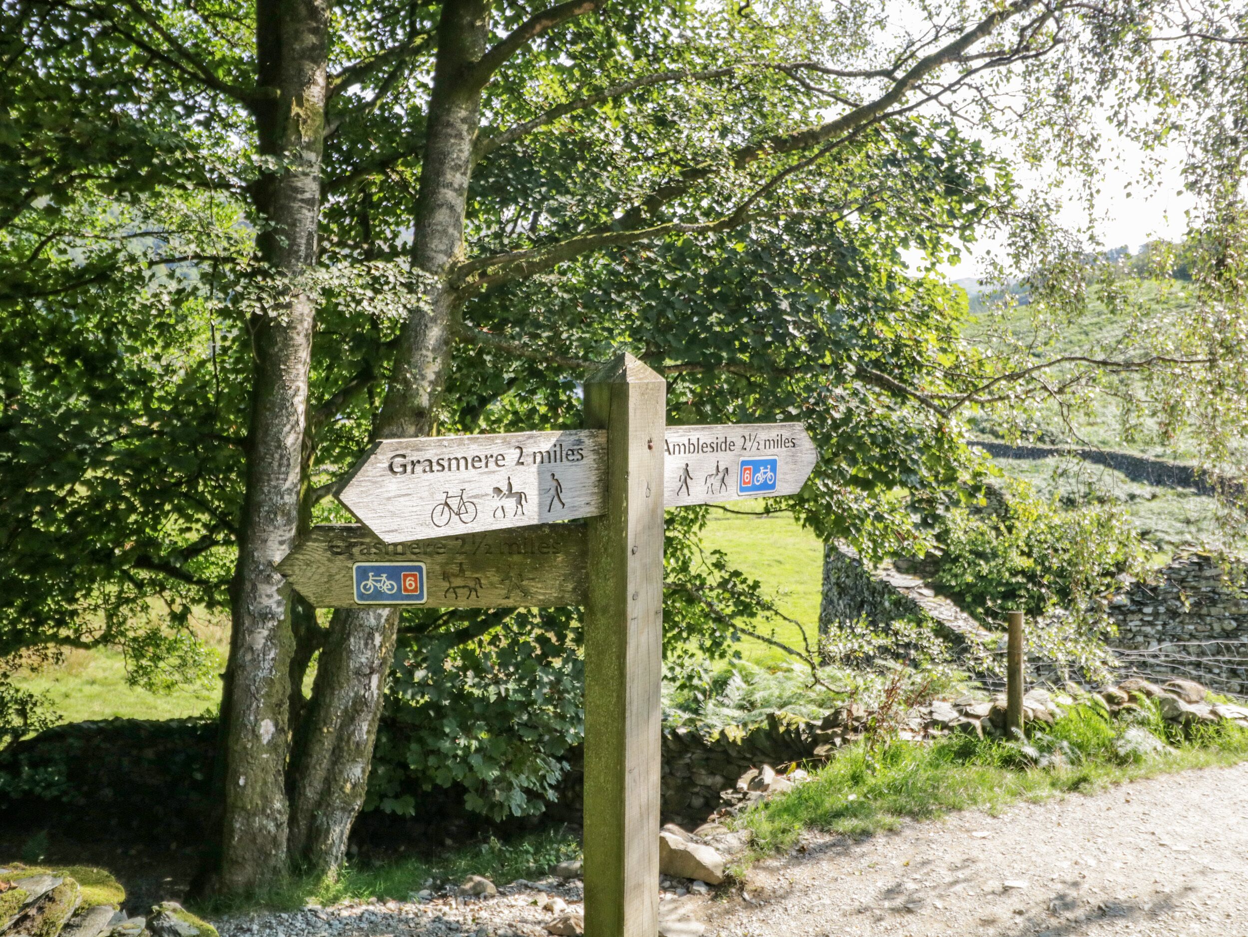 A wooden signpost with directional arrows for Grasmere and Ambleside, indicating distances and accessible routes for bicycles and pedestrians.