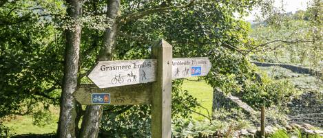 A wooden signpost with directional arrows for Grasmere and Ambleside, indicating distances and accessible routes for bicycles and pedestrians.