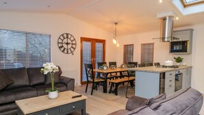 A modern living room with a sofa, a coffee table, and a dining area with a table and chairs. There is a kitchen with a microwave and a stove. - 25 Thirlmere (Windermere)