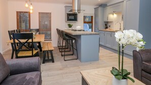 A modern kitchen with a central island, bar stools, and a dining area with a table and chairs. - 25 Thirlmere (Windermere)