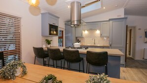 A modern kitchen with a central island, bar stools, and pendant lighting. - 25 Thirlmere (Windermere)