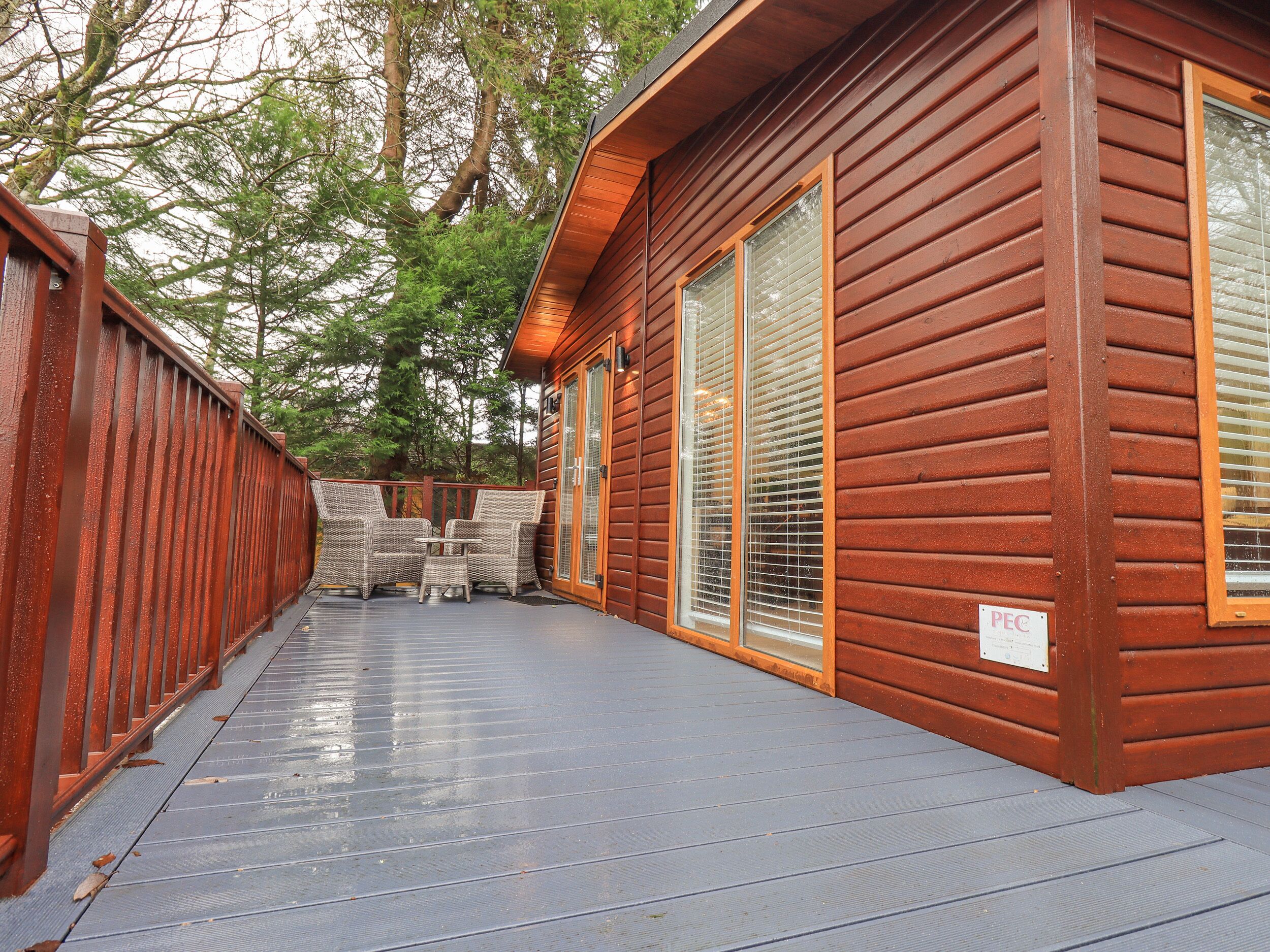 Una cabaña de madera con terraza, muebles de mimbre y ventanas amplias.