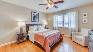 A bedroom with a bed, a ceiling fan, a nightstand, a chair, and a window with curtains. - Spacious | Quiet | 1 bedroom duplex w free parking! (St. Louis)