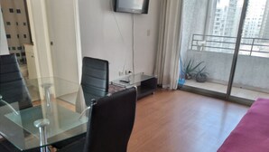 Ein modernes Zimmer mit Glastisch, schwarzen Stühlen, einem roten Bett und Blick auf Gebäude durch ein großes Fenster.