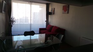 Ein Wohnzimmer mit Glastisch, rotem Sofa, Stehlampe und einem Fenster mit Vorhängen.