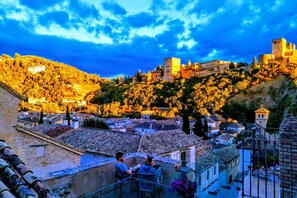 Uma cidade histórica com um castelo imponente numa colina, edifícios em terraços e vista panorâmica da cidade a partir de uma varanda.