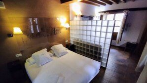 Una camera d'albergo con un letto, due lampade a parete, una finestra con tende e un muro rivestito di piastrelle.