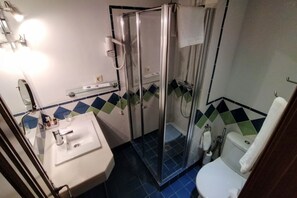 Bathroom features a glass-enclosed shower, white sink, toilet, and blue tile flooring.