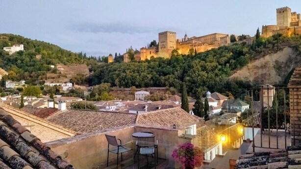 Une terrasse offrant une vue sur un château historique perché sur une colline, qui surplombe une ville aux bâtiments traditionnels.