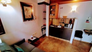 Un espace de vie compact comprenant un canapé, une petite table, un coin cuisine avec un four à micro-ondes et une chaise de salle à manger.
