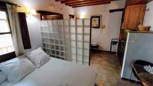Une chambre comprenant un lit, une cloison, un petit bureau et un coin cuisine.