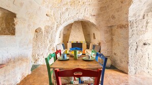A stone-walled room with a wooden table and colorful chairs. - 2530 Trullolive by Perle di Puglia (Ostuni)