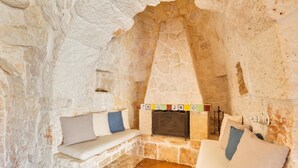A stone-walled room with a fireplace, two sofas with cushions, and a small table. - 2530 Trullolive by Perle di Puglia (Ostuni)