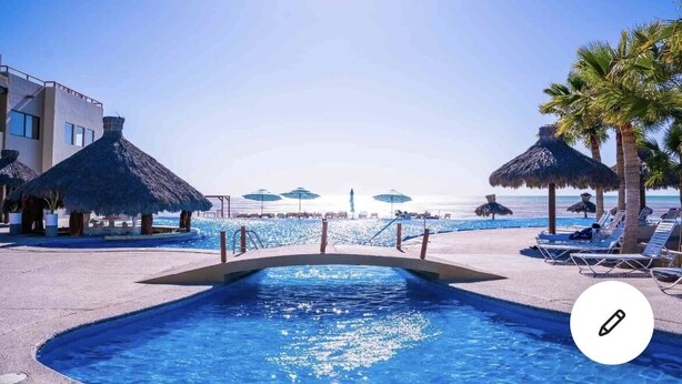 Un espace piscine avec des chaises longues et des parasols, un pont au-dessus de la piscine et une vue sur la plage.