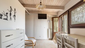 A room with a wooden ceiling, a white dresser with drawers, a bed with a wooden frame, a dining table with chairs, and a TV mounted on the wall. - 2522 Trullo Monte Cannone - Appartamento 2 by Perle di Puglia (Fasano)