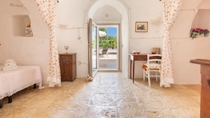 A room with a stone floor, a bed with a floral bedspread, a wooden cabinet, and a chair. - 2985 Trullo tra gli Ulivi by Barbarhouse (Carovigno)