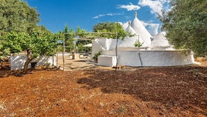 A white building with a conical roof, surrounded by trees and a clear sky. - 2985 Trullo tra gli Ulivi by Barbarhouse (Carovigno)