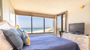 A bedroom with a large bed, a television on a dresser, and a view of the beach.