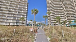 A pathway leading to a beachfront hotel with multiple balconies and palm trees.