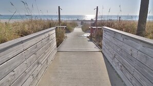 A wooden boardwalk leading to a beach with a clear sky and the sun shining.