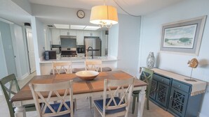 Un coin repas avec une table et des chaises en bois, un centre de table décoratif et une cuisine en arrière-plan.