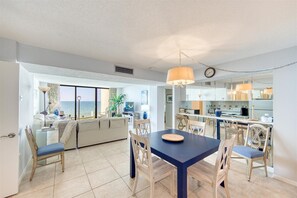 Enjoy a coastal view from the large window in this spacious living area, featuring a dining table, sofa, and TV.