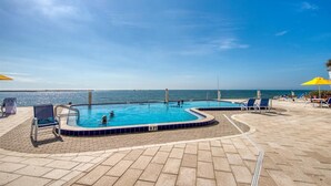 Une piscine avec vue sur la mer, entourée de chaises longues et de parasols.