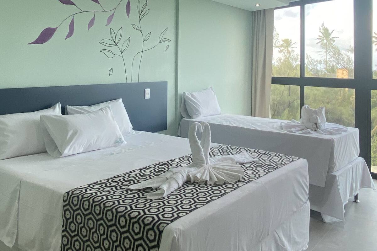 Habitación de hotel con dos camas, un ventanal grande y un mural en la pared.