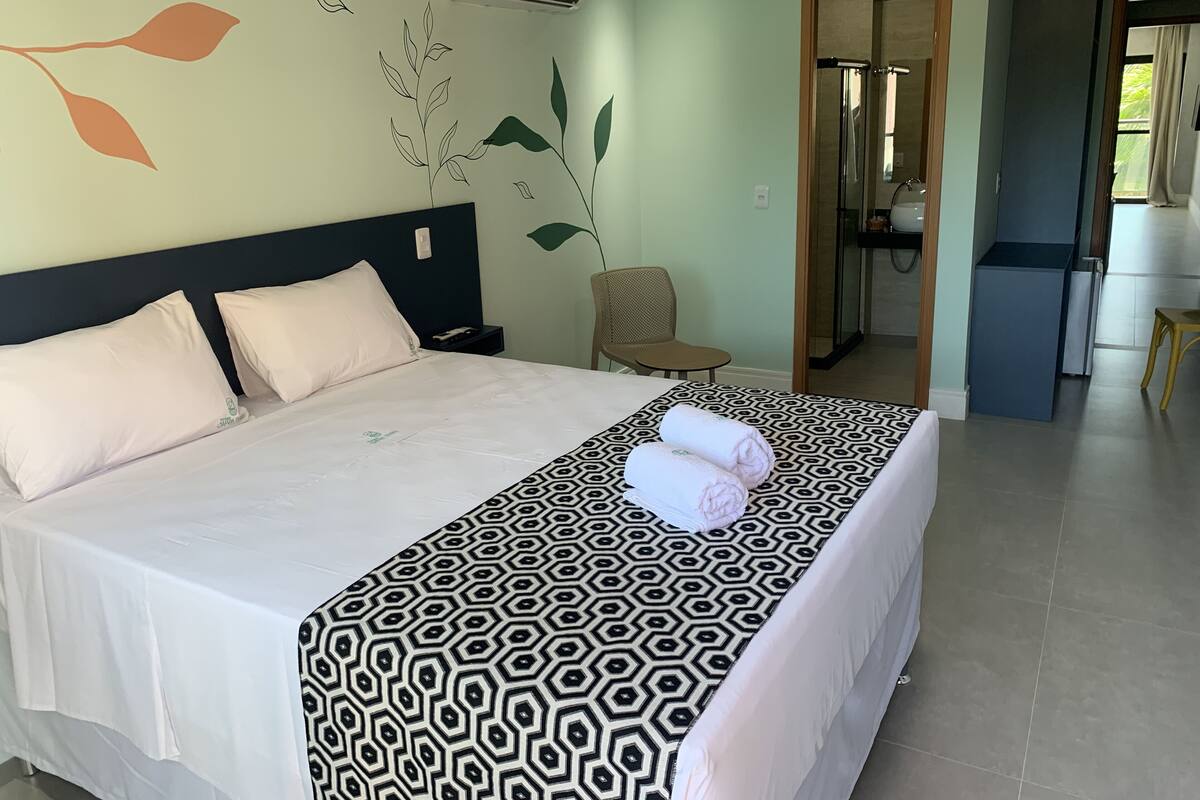 Habitación de hotel con cama, una silla, un escritorio y un baño visible a través de una puerta abierta.