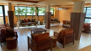 A spacious lounge area with multiple seating options including sofas and chairs, a coffee table, and a hanging swing. Large windows allow natural light to fill the space, and potted plants add greenery. - POUSADA AMADA TERRA (Ipojuca)