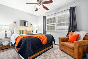 A bedroom with a bed, a nightstand, a chair, a window with curtains, and a ceiling fan. - King bed 3 bedroom Townhouse close to Toomers! (Auburn)