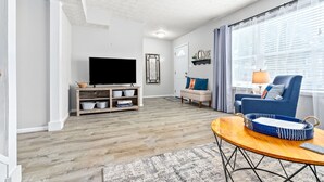 Una sala de estar con televisor de pantalla plana, un sofá, un sillón azul y una mesa de centro.