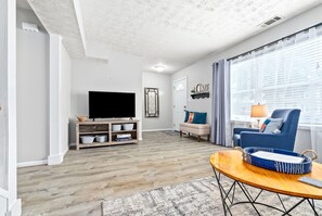 A living room with a flat-screen TV, a sofa, a blue armchair, and a coffee table. - King bed 3 bedroom Townhouse close to Toomers! (Auburn)