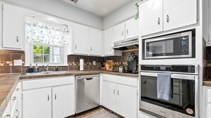 Una cocina moderna con armarios blancos, lavavajillas, microondas y horno.