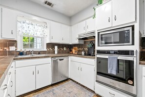 A modern kitchen with white cabinets, a dishwasher, a microwave, and an oven. - King bed 3 bedroom Townhouse close to Toomers! (Auburn)