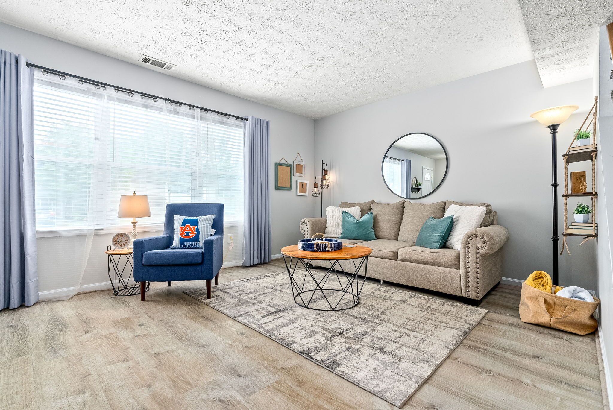 Una sala de estar con un sillón azul, un sofá beige, una mesa de centro redonda y una alfombra estampada.