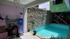 Una habitación con piso de baldosas, una pequeña piscina, una pared con diseño de roca, un ventilador de techo y un cartel en la pared.