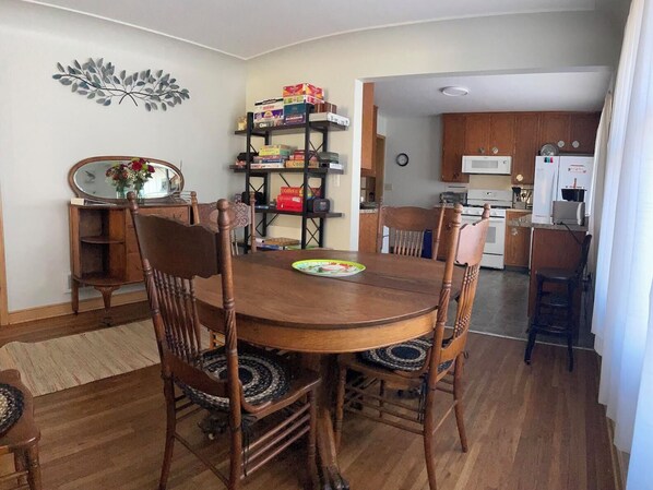 A dining area with a wooden table and chairs, a decorative wall piece, and a shelf with various items. - Clean, fun, comfy ranch home near parks, 2.5 mi to Mayo w Pingpong and Playroom (Rochester)