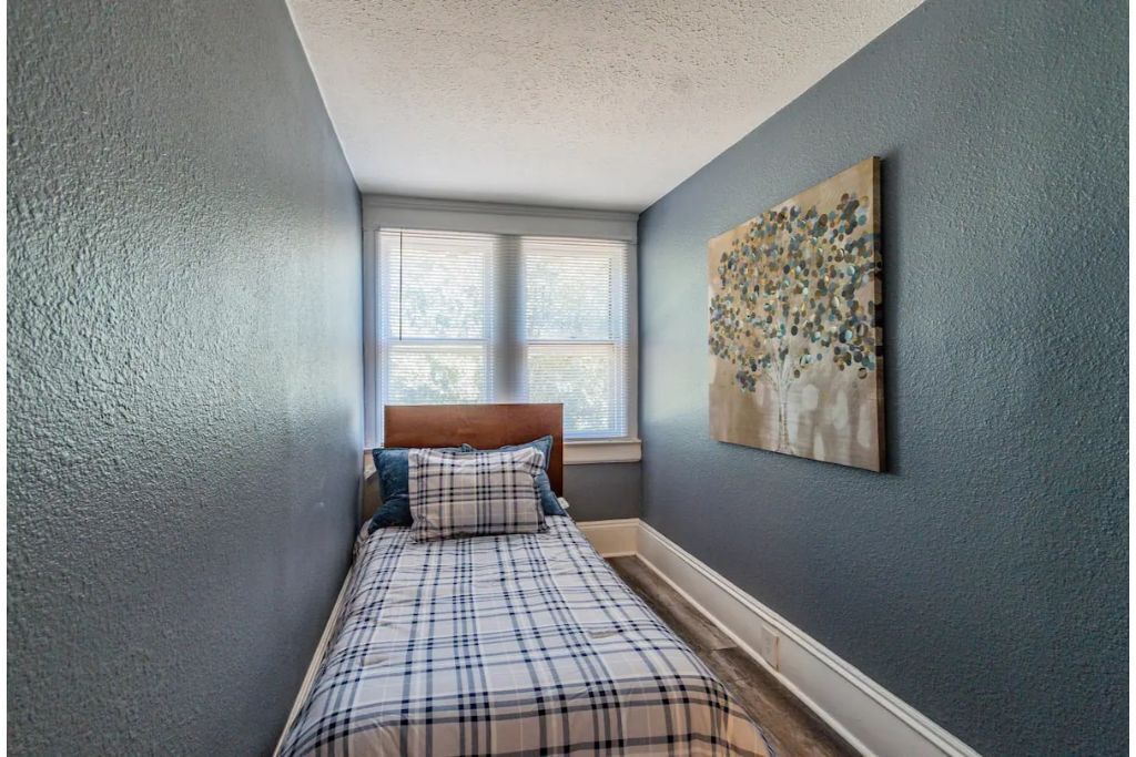 A bedroom with a bed, a window, and a wall-mounted artwork.