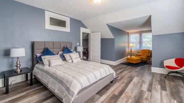A bedroom with a large bed, a nightstand, a chair, and a desk.
