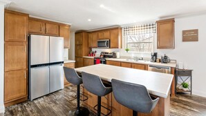 Une cuisine moderne avec des meubles en bois, des appareils électroménagers en acier inoxydable, un îlot central doté de tabourets de bar et une fenêtre offrant une belle vue.